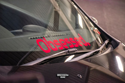 Red Obsessed heart windscreen banner fitted along the lower windscreen of a black car