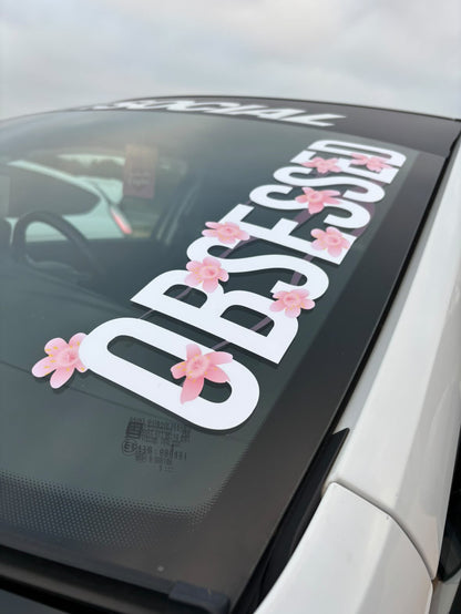 Close view of white Obsessed cherry blossom windscreen banner on a white Vauxhall Corsa