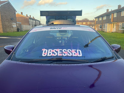 Close view of white Obsessed cherry blossom windscreen banner on a purple Renault Clio